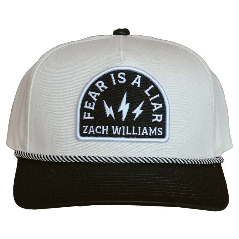 White and black baseball cap with a patch reading ’Fear is a Liar Zach Williams’.