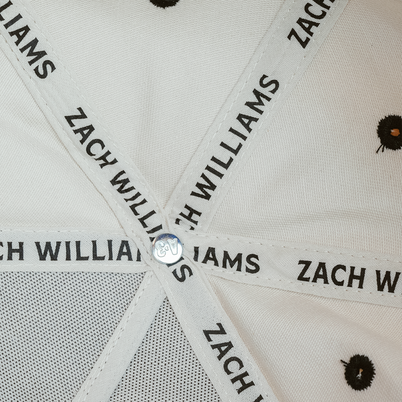 White fabric ribbons with ’ZACH WILLIAMS’ printed repeatedly, intersecting at a central point.